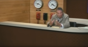 Peter Finch sitzt in seiner Rolle als "Howard Beale" in einem Nachrichtenstudio.